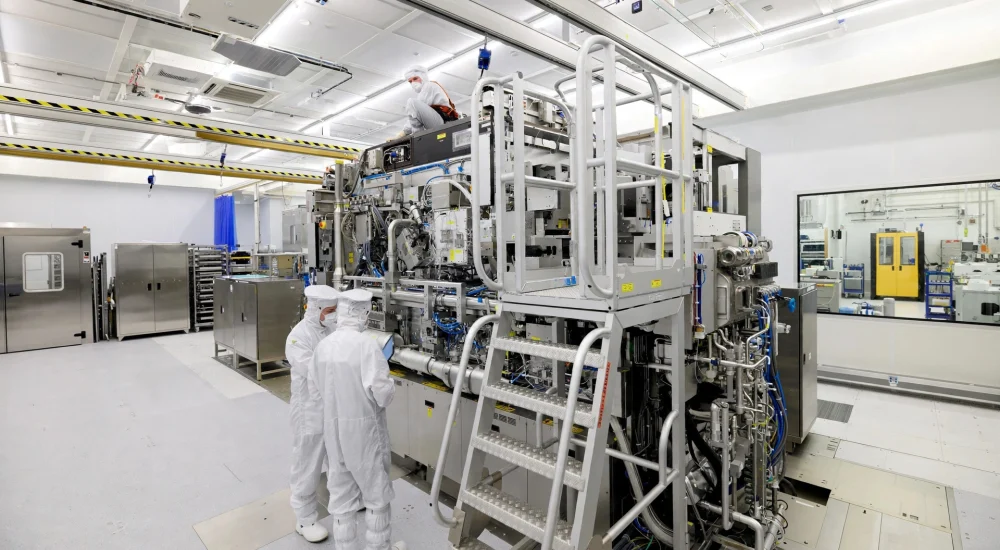 Drie medewerkers in volledige cleanroom-pakken werken aan een complexe, hightech machine voor de productie van medische hulpmiddelen in een steriele medtech-faciliteit.